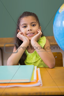 Cute pupil smiling at camera classroom with globe