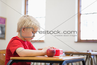 Cute pupil opening lunchbox at desk in classroom