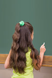 Cute pupil standing in classroom writing on chalkboard