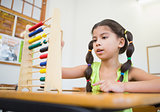 Cute pupil using abacus in classroom