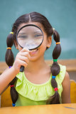 Cute pupil looking through magnifying glass in classroom