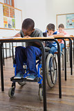 Disabled pupil writing at desk in classroom
