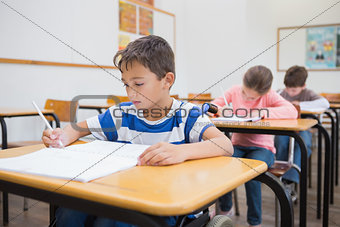 Disabled pupil writing at desk in classroom