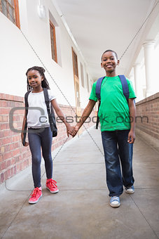 Cute pupils holding hands in corridor