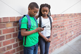 Cute pupils looking at smartphone in corridor