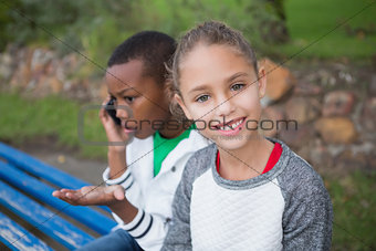 Cute little girl smiling at camera while friend talks on phone