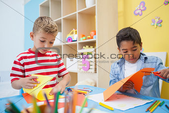 Cute little boys cutting paper shapes in classroom