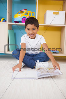 Cute little boy sitting on floor reading in classroom
