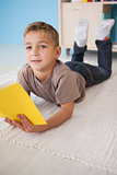 Cute little boy sitting on floor reading in classroom