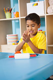 Cute little boy playing with modelling clay in classroom