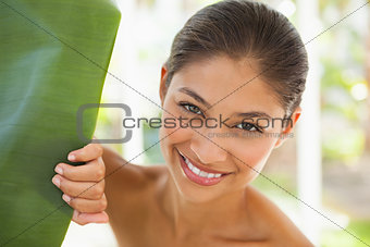 Beautiful brunette smiling at camera behind leaf