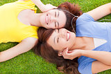 two pretty young woman lying on grassland and listening music 
