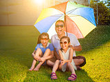 Father and daughters sitting on a meadow with colorful umbrella