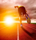 Athletic young man running on race track with sunset background