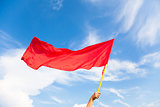 Hand waving a red flag with blue sky background
