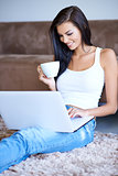 Woman drinking coffee as she types on her laptop