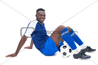 Football player in blue sitting with ball