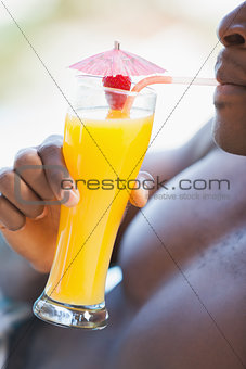 Shirtless man drinking orange cocktail