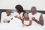 Family relaxing together in bed having breakfast