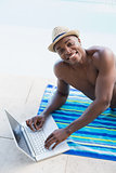 Handsome shirtless man using laptop poolside