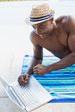 Handsome shirtless man using laptop poolside