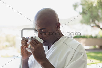 Handsome man in bathrobe drinking coffee outside