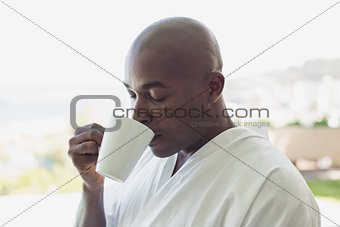 Handsome man in bathrobe drinking coffee outside