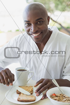 Handsome man in bathrobe having breakfast outside
