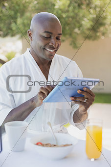 Handsome man in bathrobe using tablet at breakfast outside