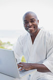 Handsome man in bathrobe using laptop outside