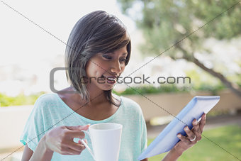 Pretty woman having her coffee outside using tablet pc