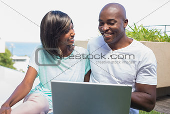 Happy couple sitting in garden using laptop together
