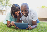 Happy couple lying in garden using tablet pc together