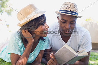 Happy couple lying in garden together reading book