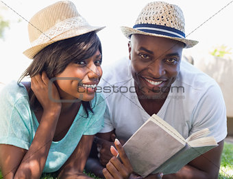 Happy couple lying in garden together reading book