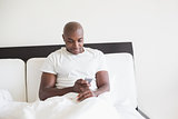 Happy man sitting in bed using smartphone