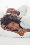 Upset woman lying in bed with sleeping boyfriend