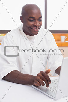 Happy man in bathrobe using laptop at table
