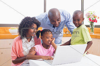 Cute siblings using laptop together with parents