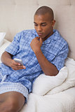 Thoughtful man sitting on bed sending text