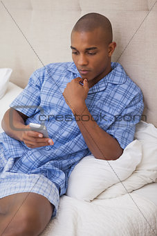 Thoughtful man sitting on bed sending text