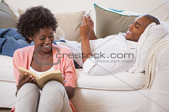 Happy couple relaxing together reading book and using smartphone