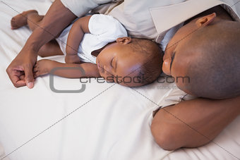 Father napping with baby son on couch