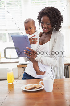 Happy mother holding baby son while using tablet pc