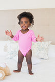 Baby girl in pink babygro standing on bed