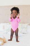 Baby girl in pink babygro standing on bed