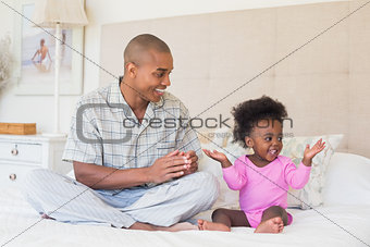 Happy father and baby girl sitting on bed together