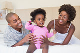 Happy parents playing with baby girl on bed together