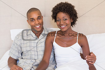 Happy couple sitting on bed smiling at camera