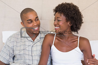 Happy couple sitting on bed smiling at each other